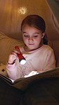 Girl, kid and reading book with torch at night for fairy tale or bedtime story at home. Child, relax and late evening with light or flashlight for novel, imagination or literature in bedroom at house
