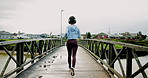 Back, running and woman in city, fitness and cardio with training with wellness, energy and exercise. Outdoor, person and runner with headset, muscle development and health with challenge or New York