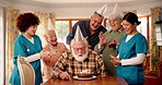Senior man, birthday cake and blow candles in nursing home for celebration. Party, retirement and special event with dessert, social gathering or singing with happy friends or medical team clapping