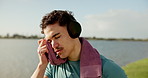 Fitness, music and sweating with man outdoor for break from cardio challenge or intense training. Headphones, thinking and towel with tired athlete at lake for exercise or recovery from workout