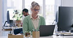 A mature blonde businesswoman wearing spectacles working in her office using a laptop while sitting at a desk. Female secretary doing admin work and looking focused while doing her job