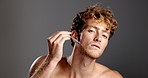 Face, skincare and man with serum for beard, shine and glow on gray studio background. Portrait, pipette and happy model apply cosmetics product for hydration, vitamin c treatment and essential oil