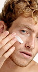 Man, skincare and cream for face in studio with application, cosmetics or product by white background. Person, facial lotion or moisturizer in portrait for routine, dermatology and beauty in Germany