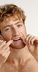 Dental care, floss and face of man in studio for hygiene, plaque removal or grooming in morning. Oral health, wellness and person with string for cleaning teeth or fresh breath by white background.