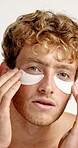 Man, face or under eye patches in studio for skin hydration, puffiness reduction or dark circles. Skincare, person or happy with cosmetic pads for anti aging benefits or self care on white background