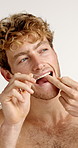 Dental health, floss and man in studio for hygiene, plaque removal or grooming in morning. Oral care, wellness and male person with string for cleaning teeth or fresh breath by white background.