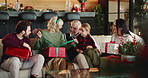 Happy, big family and christmas with box for gift giving, presents or surprise together in home. Grandparents, parents and child with unwrapping or ribbon on sofa for christian tradition in house