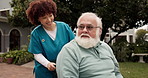 Caregiver, walking and old man with wheelchair in garden for medical support, fresh air or talking. Healthcare, nurse or senior person with disability for rehabilitation or service at retirement home