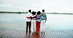 Back, friends and hug at lake for holiday, vacation and travel together on trip outdoor with space. Water, pier and group of people embrace for reunion, view and adventure with students on gap year