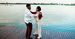 Couple, dancing and happy by lake, vacation and rhythm with connection, trust and love in summer. African man, woman and partner with holding hands, conversation and smile with romance at park