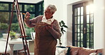 Painting, woman and creative in home, smile or artist with paint brush for artwork, talent or craft. Happy, elderly person and inspiration for project, canvas and process with watercolor in lounge