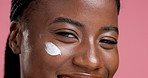 Face, black woman and lotion for beauty in studio for skincare, facial hydration and shine. Smile, female person and spf cream of moisturiser benefits, treatment glow and self care on pink background