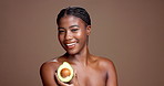 African woman, avocado and face in studio for beauty, happy and nutrition for skincare by background. Girl, model and smile in portrait for wellness benefits, fruit diet and mockup space in Nigeria