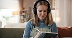 Education, music and tablet with woman on sofa in living room of home for distance learning. App, headphones and writing with college student in apartment for remote study or university course