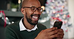 Happy, black man and texting with phone for christmas celebration or december holiday in home. Excited, male person and laughing with mobile smartphone for online chatting, new year or joke in house