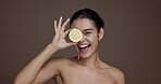 Face, woman and lemon eyes for skincare in studio for vitamin c, brighten skin and natural detox. Portrait, person and citrus fruit for organic benefits, beauty and treatment glow on brown background