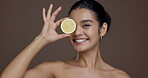 Face, woman and fruit for skincare in studio for vitamin c, brighten skin and natural detox. Portrait, person and citrus lemon for organic benefits, beauty and exfoliate treatment on brown background
