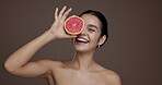 Face, woman and grapefruit for skincare in studio for vitamin c, brighten skin and natural detox. Portrait, person and fruit with organic benefits, beauty and exfoliate treatment on brown background