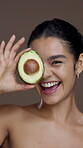Avocado, skincare and smile with face of woman in studio for natural beauty, self care and cosmetics. Glow, omega 3 benefits and vitamin e with person and fruit on brown background for antioxidants