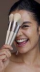 Brushes, makeup and face of woman in studio for grooming, foundation or facial glow with smile. Happy, cosmetic tools and portrait of female person from Mexico with cosmetology by brown background.