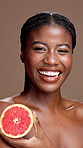 Black woman, face or skincare with grapefruit for health or vitamin C on a brown studio background. Portrait, female person or happy model with smile or natural organic fruit for antioxidant or fiber