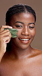 Beauty, face and gua sha with black woman in studio for natural skin treatment or wellness. Facial massage, jade stone and smile of model person on brown background for cosmetic dermatology routine