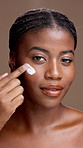 Face, skincare and black woman with cream application for beauty, sunscreen and laugh. Portrait, cosmetics and smile with lotion for dermatology, shine and hyaluronic acid on brown studio background