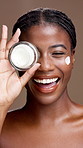Face, skincare cream and black woman with product for beauty, glow and laugh. Portrait, cosmetics jar and smile with moisturizer for dermatology, shine and hyaluronic acid on brown studio background