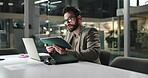 Man, reading and tablet in office at night for accounting, finance planning and budget report. Male person, laptop and  charts of financial comparison, profit and information for investment deadline