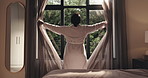 Back view, woman and curtains in hotel room for morning routine, wake up and getting ready for trip. Tourist, hospitality and new day in bedroom of resort for travel, vacation and holiday with robe