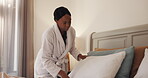 Pillow, black woman and making bed in hotel room for morning routine, maintenance and getting ready. Tourist, hospitality and cleaning in bedroom of resort for travel, vacation and holiday with robe