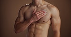 Hand, cream and man in studio, cosmetics and applying with dermatology on brown background. Closeup, beauty and person with skincare, creme and lotion with chest, muscular and moisturizing with shine