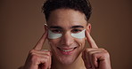 Face, eye patches and man with cosmetics, smile and beauty on brown studio background. Portrait, space and happy person with dermatology, spa wellness or grooming with routine, aesthetic or treatment