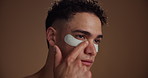 Cosmetics, eye patches and man in studio, skincare and dermatology on brown background. Beauty, space and person with healthy skin, spa wellness and grooming with routine, aesthetic and treatment