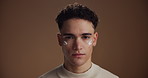 Face, cream and man in studio, dermatology and grooming with beauty on brown background. Creme, space and happy person with wellness, skincare and cosmetics with aesthetic, lotion and treatment