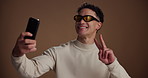 Selfie, funny and man in studio, glasses and confidence with fashion influencer on brown background. Space, content creation and person with happiness, humor and smile with pride, eyewear and trendy