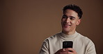 Thinking, smartphone and man in studio, typing and social media with app on brown background. Mobile user, space and happy person with cellphone, solution and message to contact, chatting and ideas