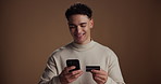 Funny, credit card and man in studio, smartphone and payment with online banking on brown background. Space, cellphone and person with ecommerce, transactions and fintech with smile and discount deal