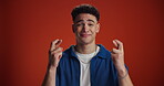 Wish, face and student with fingers crossed in studio for exam results, positive outcome or hope. Mockup, nervous man or good luck on red background for scholarship acceptance, test grade or suspense