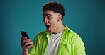 Happy, man and surprise with phone in studio for good news, lottery winner or online announcement. Excited, person and celebration with smartphone on blue background for giveaway or competition promo