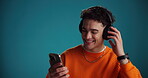 Phone, man and dancing with headphones in studio for music playlist, hip hop track and subscription. Rhythm, person and happy with smartphone for listening to online song and audio on blue background
