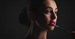 Woman, brush and lipstick in studio for beauty, cosmetics or color application process on black background. Girl, cosmetology tools and red lips with facial makeup, self care and glow with product