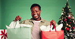 Christmas, shopping and face of black man in studio with gifts, tradition or bags for holiday discount. Happy, customer and excited male person with retail sale for xmas presents by green background.