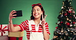 Christmas, woman and selfie with peace sign in studio for holiday memory, festive season and vlog. Influencer, girl and  wink with photography on green background for xmas celebration or social media