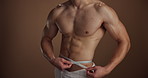Tape measure, closeup and man in studio, weight loss and workout on brown background. Muscular, bodybuilder and person with fitness, abs and diet with nutrition, mockup space or results with wellness