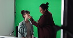 Woman, news reporter and makeup artist with green screen, brush and lipstick at studio for television. Person, speaker or presenter with cosmetics, application or behind the scenes for tv broadcast