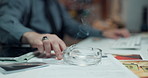 Officer, hands and smoking with cigarette on desk for private investigation, stress or nicotine. Person, detective or smoker with ash tray at night for crime scene research, evidence or serial killer