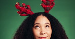 Christmas, antlers and woman in studio, thinking and tradition on green background. Xmas, holiday season and person with reindeer ears, headband and decision with wonder, choice and thoughtful