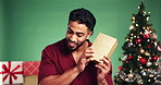 Shaking, present and man with smile, Christmas and excited with box, festive season and celebration. Curious, person and guess xmas gift, studio or happy for holiday, listening and green background