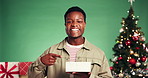 Christmas, gift and pointing with face of black man in studio for celebration, promotion and holiday season. Surprise, festive event and xmas with person on green background for December present